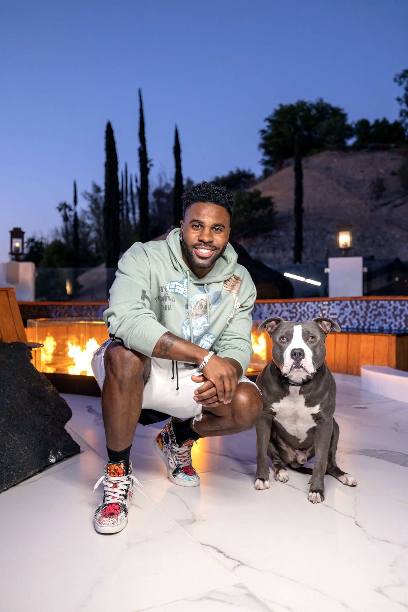 Jason Derulo and his canine companion, Ice, in front of his outdoor firepit with flooring made of white & gray vein porcelain slab that looks like marble.