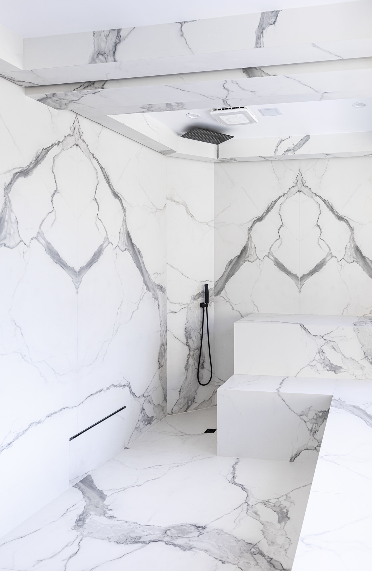 Steam room with black fixtures and white with gray veining porcelain slab that looks like marble.