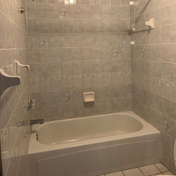 Before photo of shower/bathtub combination with gray shower wall tile with painted flowers, light gray bathtub, and gray floor tile.