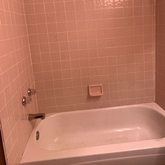 Before photo of shower/tub combination with square pink shower wall tile, pink wall-mounted soap dish, and pink bathtub.