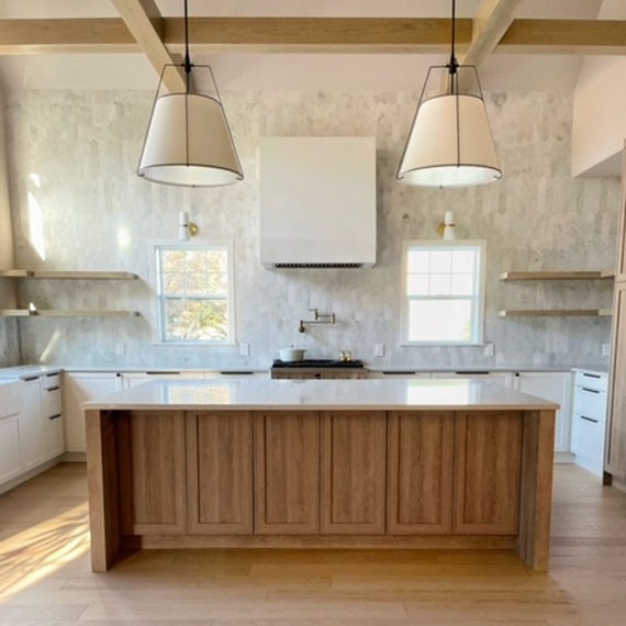 Recently renovated kitchen with white & gray picket marble wall tile, floating shelves, white quartz countertops, wood island, and ceiling with beams.