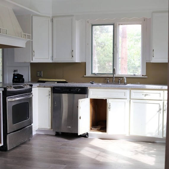 Before photo of kitchen with brown walls, gray speckled Formica countertops, white upper and lower cabinets.