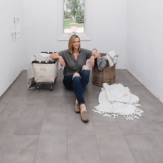 Jennifer GizziInstagram influencer Jennifer Gizzi sitting on gray concrete-look floor tile, in her laundry room that is in the process of being renovated.