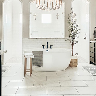Newly renovated bathroom with white & gray floor tile that looks like marble, soaker tub with black faucet and white backsplash, large shower with dual showerheads.