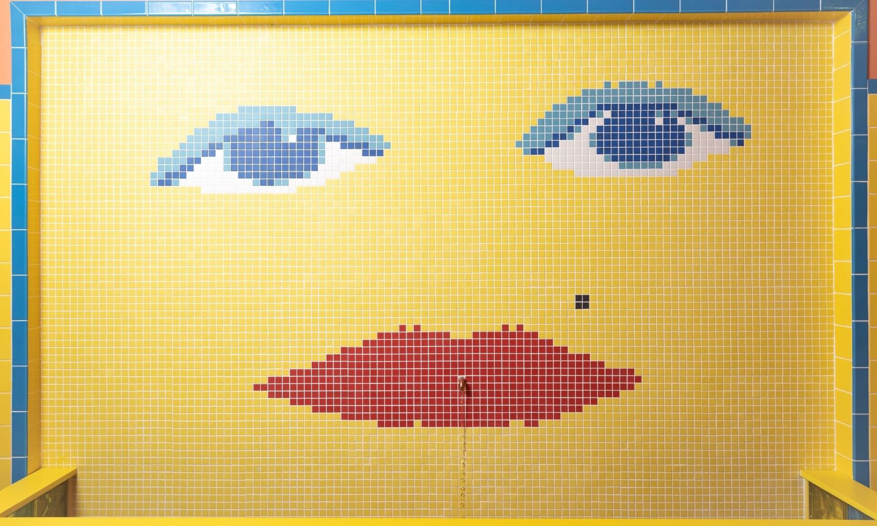 Wall fountain with yellow, blue, white, and red mosaic wall tile that looks like a woman's face.