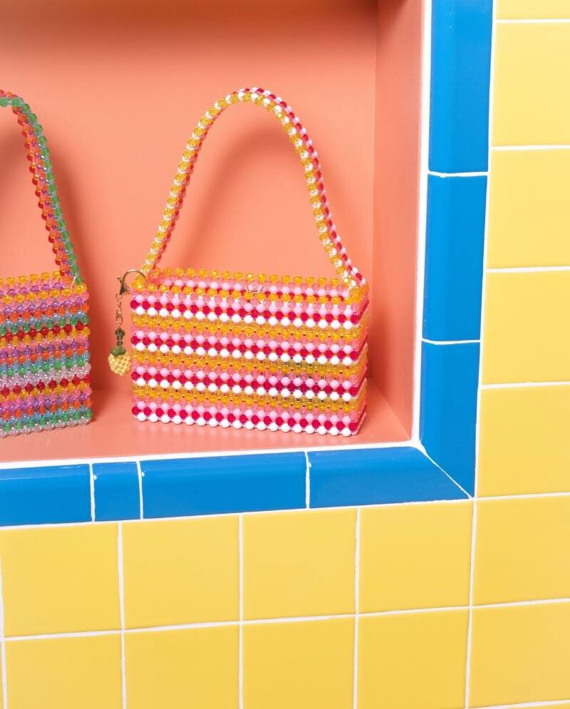 Susan Alexandra yellow, white, light pink & bright pink beaded purse on wall niche surrounded by bright blue bullnose tile and bright yellow wall tile.