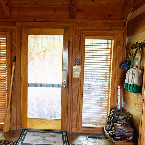 Before photo of home entrance with natural wood walls and ceiling, glass door with 2 side windows, and stone mosaic flooring.