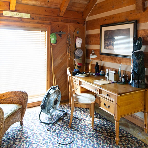 Before photo of home office with natural wood walls and ceiling, blue, tan, and white mosaic flooring, wood desk and chair.