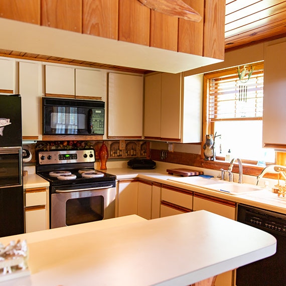 Before photo of kitchen with white cabinets, white countertops, natural wood ceiling, and sink in front of a window.