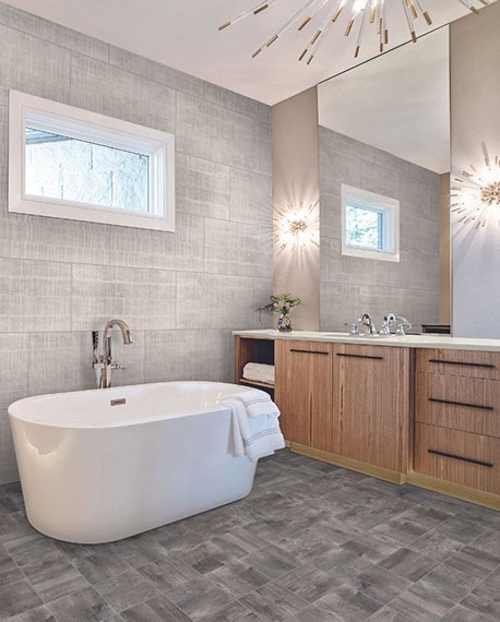 Bathroom with seasoned wood look floor tile, gray fabric look wall tile, soaker tub, separate natural wood vanities with white quartz counters, starburst lighting.