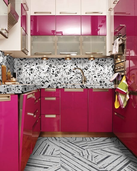 Small apartment kitchen with bright pink cabinets with brass accents, white & black porcelain slab backsplash that look like terrazzo, black & white striped floor tile.