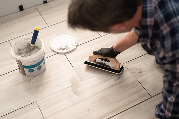 Overhead view of man grouting stone look click tile with RapidGrout and a trowel. 