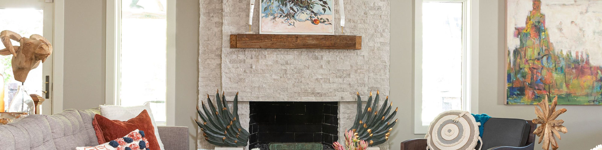 Rustic fireplace with split-face cream limestone tile façade, wood mantle, honed limestone hearth holding pair of green sculptures.