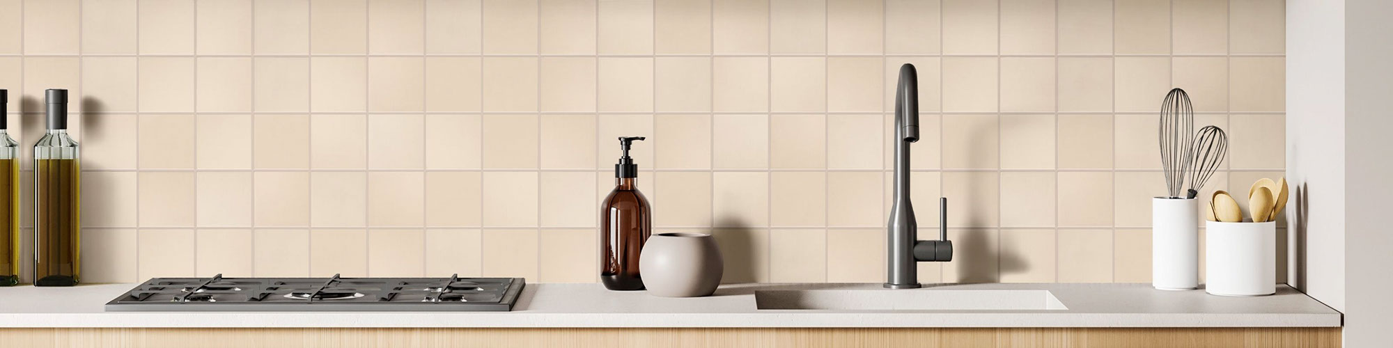Closeup of kitchen backsplash of cream wall tile, undermount sink with gray faucet, brown glass soap dispenser, and white containers of kitchen utensils.