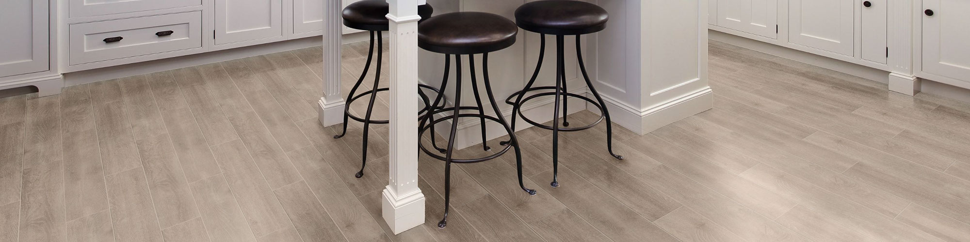 Eat-in kitchen with island with white base, floor tile that looks like blonde wood flooring, brown leather & black metal bar stools.