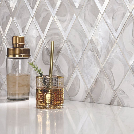 Dry bar with white & gray diamond-shaped backsplash, gold trimmed hi-ball glass and shaker on a white quartz countertop.