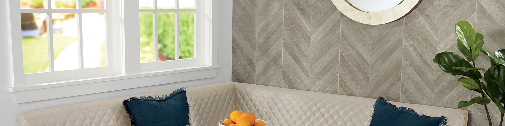 Closeup of wall tile that looks like wood, laid in a chevron pattern, beige tufted booth with navy pillows, white framed windows.