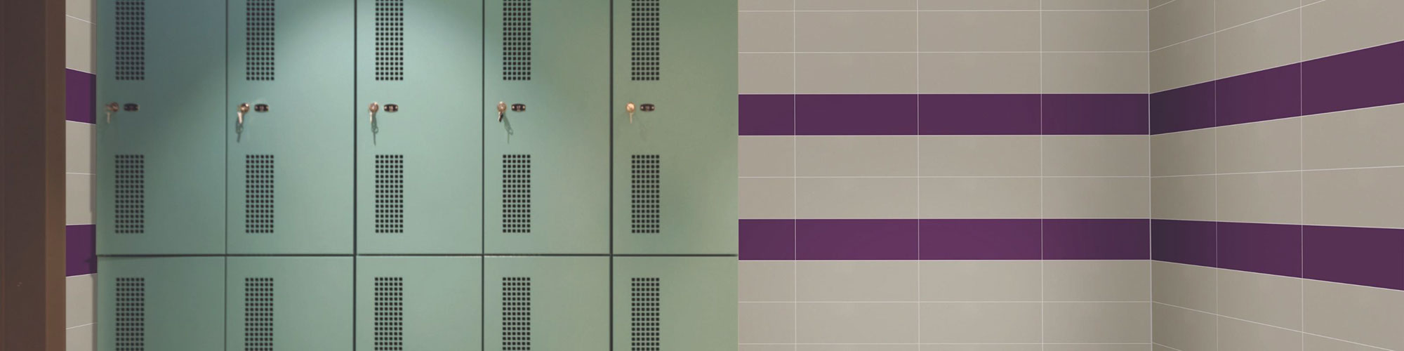 Locker room with beige wall tile with 2 purple horizontal stripes and mint green lockers.