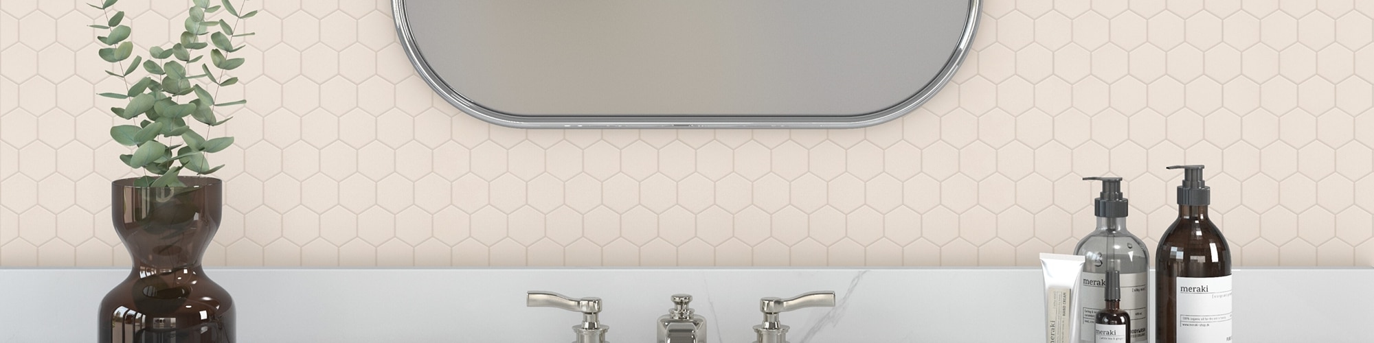 Bathroom vanity area with off-white hexagon mosaic tile backsplash, silver framed mirror, vase holding eucalyptus leaves, pump lotion and hand soap.