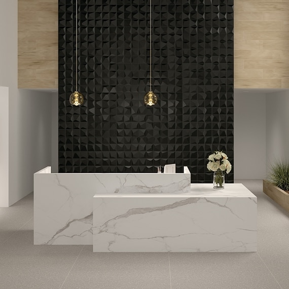 Office building lobby with white and gray marble look porcelain slab reception desk, feature wall with textured glossy black tile, and gray fabric look tile flooring.