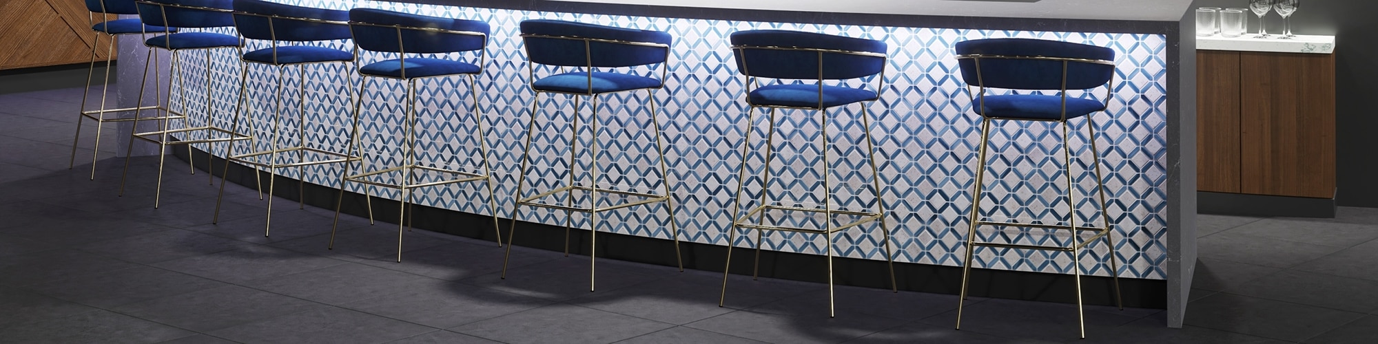 Nightclub bar with dark gray floor tile that looks like concrete, bar base with white and blue lattice mosaic tile, and blue & brass bar stools.