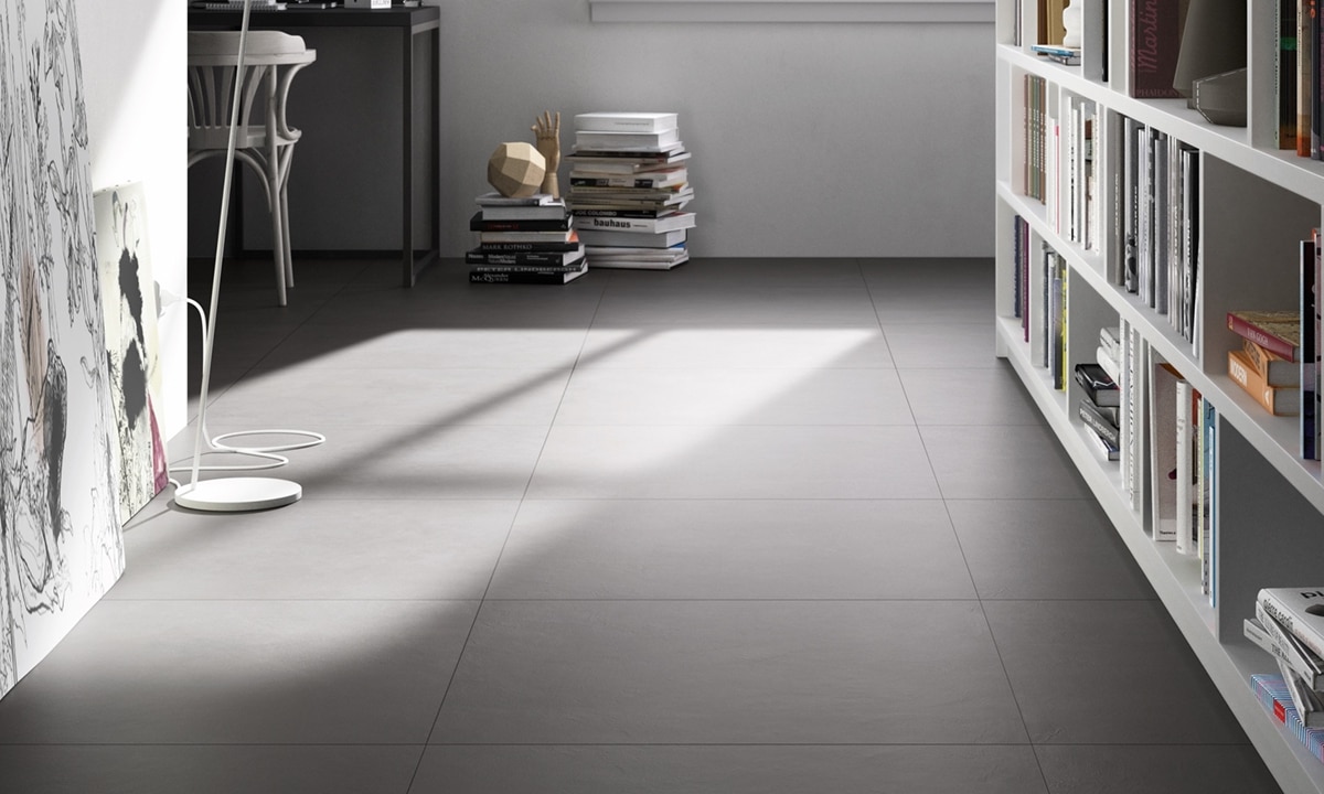 Hallway with dark gray floor tile that looks like concrete, white bookshelves, small desk next to a stack of books under picture window. 