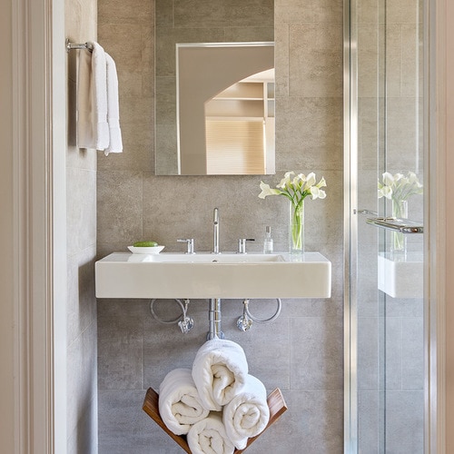 Small gray bathroom with towel rack and rolled towels under the sink